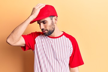 Young handsome man with beard wearing baseball cap and t-shirt surprised with hand on head for mistake, remember error. forgot, bad memory concept.