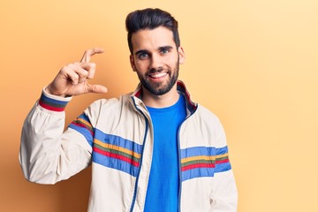Young handsome man with beard wearing casual jacket smiling and confident gesturing with hand doing small size sign with fingers looking and the camera. measure concept.