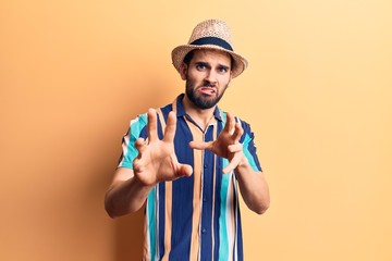 Young handsome man with beard wearing summer hat and shirt disgusted expression, displeased and fearful doing disgust face because aversion reaction. with hands raised