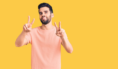 Young handsome man with beard wearing casual t-shirt smiling looking to the camera showing fingers doing victory sign. number two.