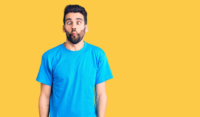 Young handsome man with beard wearing casual t-shirt making fish face with lips, crazy and comical gesture. funny expression.