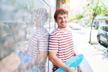 Young caucasian skater man smiling happy holding skate leaning on the wall city. © Krakenimages.com