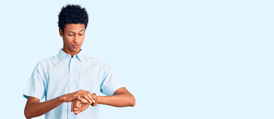 Young african american man wearing casual clothes checking the time on wrist watch, relaxed and...