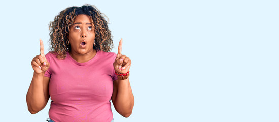 Young african american plus size woman wearing casual clothes amazed and surprised looking up and pointing with fingers and raised arms.