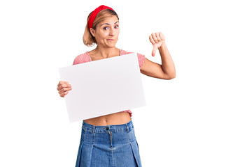 Young blonde woman holding blank empty banner with angry face, negative sign showing dislike with...