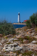 Fototapeta na wymiar White stone lighthouse stands on the seashore