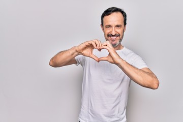 Middle age handsome man wearing casual t-shirt standing over isolated white background smiling in love doing heart symbol shape with hands. Romantic concept.