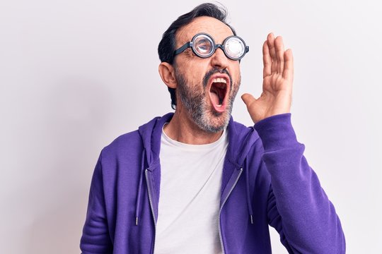 Middle age handsome freaky man wearing dumb glasses over isolated white background shouting and screaming loud to side with hand on mouth. Communication concept.