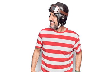 Middle age aviator man wearing vintage helmet and glasses over isolated white background looking to side, relax profile pose with natural face and confident smile. © Krakenimages.com
