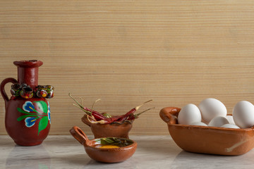 Vasija de barro huevos blancos, chies de árbol y una jarra de barro decorada, sobre una barra de...