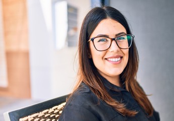 Young beautiful brunette woman wearing glasses smiling happy and confident. Sitting with smile on face at restaurant