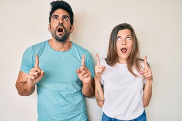 Beautiful young couple of boyfriend and girlfriend together amazed and surprised looking up and pointing with fingers and raised arms.