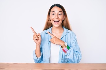 Young brunette woman sitting on the table wearing casual clothes smiling and looking at the camera...