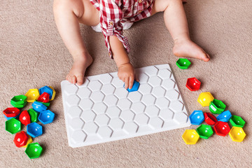 A toddler plays with a plastic mosaic on the carpet in the children's room. Early development, the Montessori method.