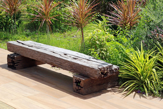 Bench made from an old wooden railway sleeper with a background of a green tropical garden in bright sunshine