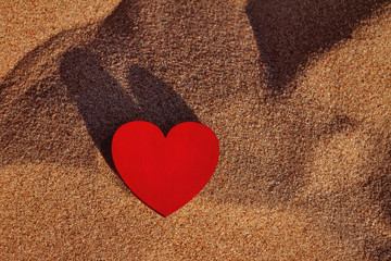Fototapeta premium wooden red heart lies on golden sand on beach, copy space