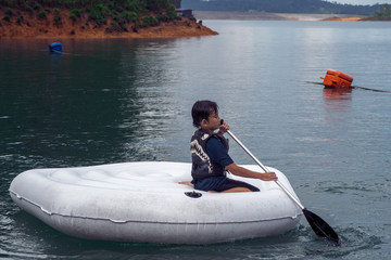 Family wearing life jackets paddling on an inflatable boat in Kenyir Lake, Malaysia.