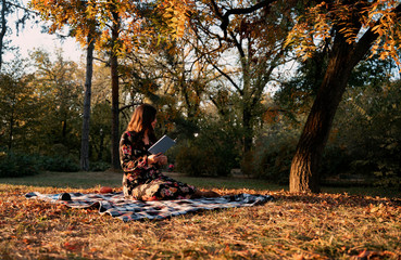 Artistic image, young woman sitting on blanket in the morning in park and reading a book 