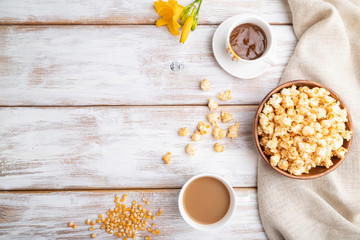 Popcorn with caramel in wooden bowl and a cup of coffee on a white wooden background. Top view, flat lay, copy space.