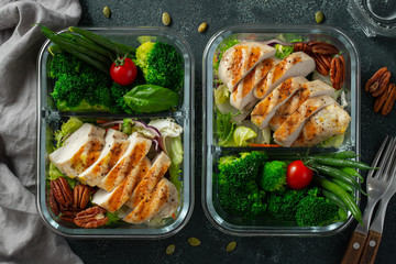 Healthy meal prep containers with green beans, chicken breast and broccoli. A set of food for keto diet in lunchbox on a dark concrete background. Top view