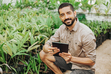 Latin man working in his seedling nursery using digital tablet. Small business owner concept.