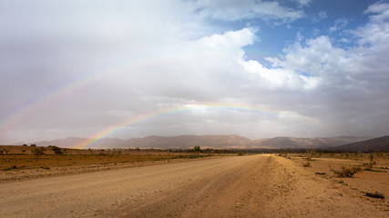 Double rainbow at the desert after the rain. Unsealed road suitable for 4wd cars. Dramatic sky with dark clouds. Mountains at the background covered by the fog. Flinders Ranges, South Australia