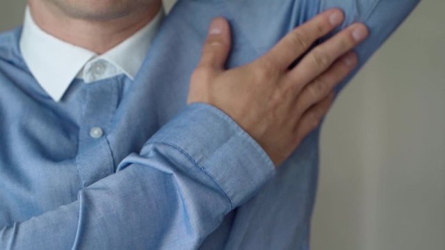Male Wearing Blue Shirt Lifting Up Left Arm And Touching Sweat Patch With Hand. Locked Off 