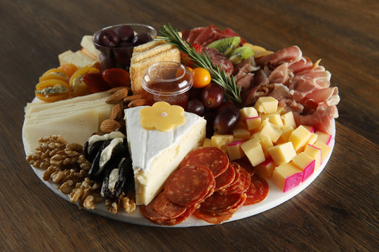 Brie, gouda, asiago, parmesan, cup, salami, jamon, apricots with gorgonzola, plums with cream chease and fruit. Antipasto dish on wooden table. Selective focus