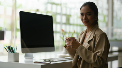 Portrait of female entrepreneur smiling while relaxing with a cup of beverage at workplace