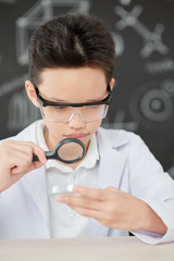 Curious Asian schoolboy looking at petri dish through magnifying glass