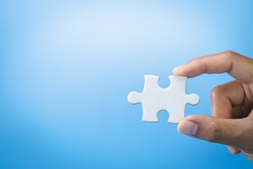 Hand holding jigsaw puzzleson a blue background, Business solutions, success and strategy concept.