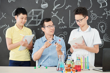 Young Asian science teacher showing plastic model of chemical molecule to curious school children...