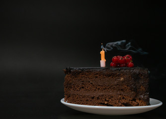 Piece of chocolate birthday cake with one extinguished candle on white plate on deep black...