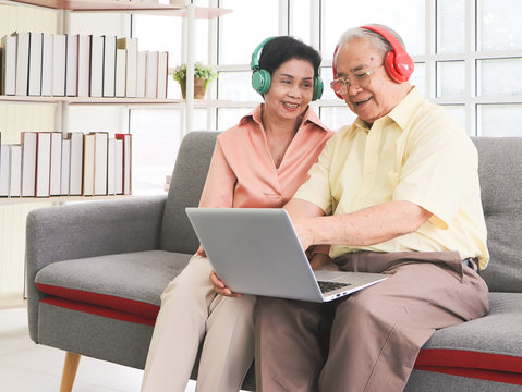 Asian Senior Couple Having Goodtime Together , Listen To The Music From Headphones With Computer Laptop On Lap. Elderly Lifestyle Concept.