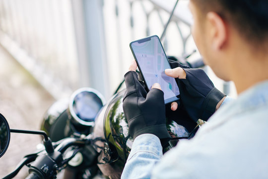 Motorcyclist in fingerless gloves checking map on smartphone screen before riding to destination point