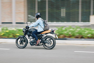 Young man in helmet with backpack riding fast on motorcycle along city roads