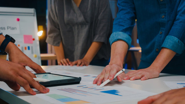 Millennial Asia businessmen and businesswomen meeting brainstorming ideas about new paperwork project colleagues working together planning success strategy enjoy teamwork in small modern night office.