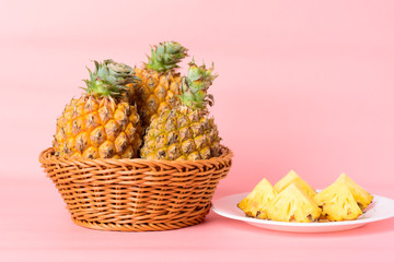 Sliced pineapple fruit on white plate and basket on pastel pink background, Tropical fruit