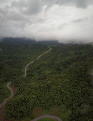 Logistic concept aerial view of countryside road - motorway passing through the serene lush greenery and foliage tropical rain forest mountain landscape