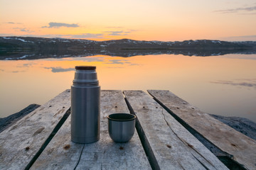 Sunset  bay  calm water  wooden pier  thermos with tea on the pier.