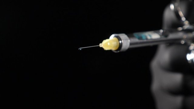 Dentist hand in black glove holding syringe with anesthesia Releasing Drug drop by drop. Usage of Sterile Equipment. Close-up shot of dentist holding syringe with anesthetic on black background. Full