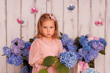 Happy baby girl in a dress in the studio on a white background with pink and blue hydrangea flowers