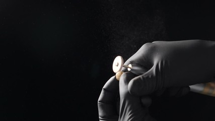 Close-up view of dental technician holding dental crown work and drill in his hands and creating dentures in laboratory. Dental concept shot on black background. Slow motion full hd video