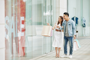 Young Vietnamese couple shopping in mall on weeked, walking and looking through shop window