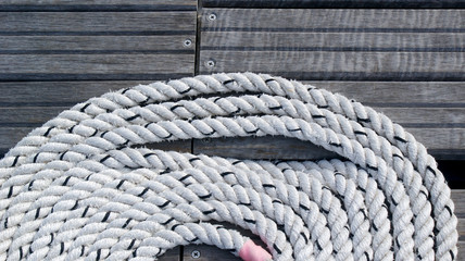 strong white nautical rope in a circle around a pier on the background of wooden boards
