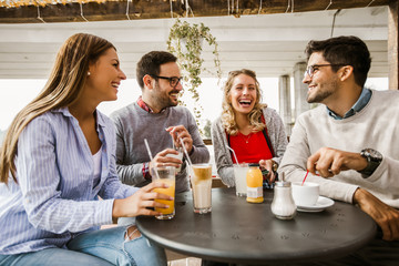 Group of four friends having fun a coffee together. Two women and two men at cafe talking laughing and enjoying their time