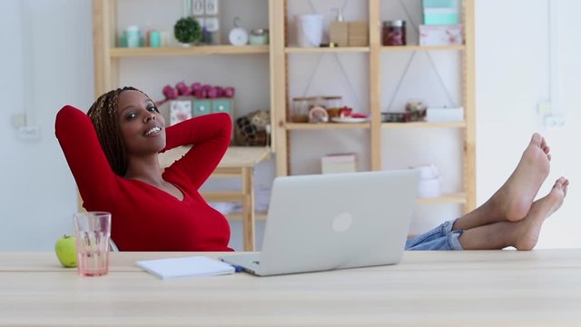 woman with resting her legs on the table at home office, look at camera portrait Spbi. african american young girl student freelancer finished work, study. concept dreamlike