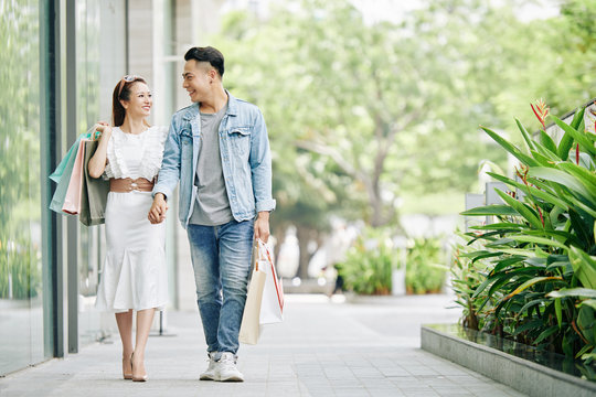 Happy young Vietnamese couple holding hands when walking in the street after shopping