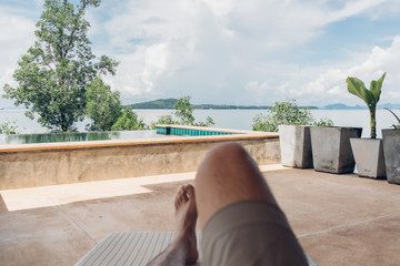 Legs shot of man lying on the bench relax with the sea view in the house.