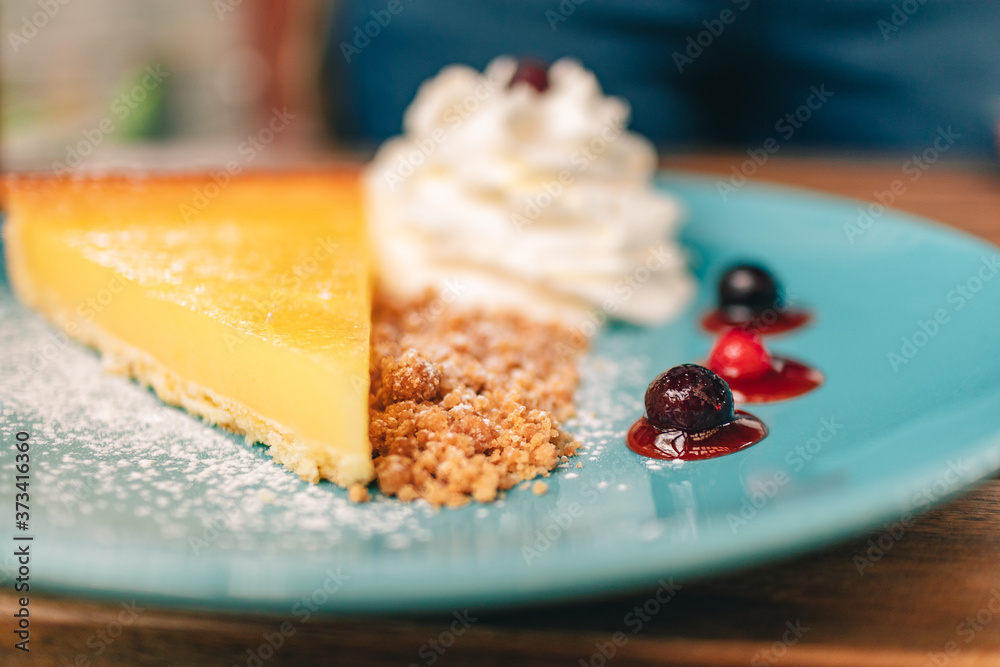 Wall mural small slice of lemon cheesecake with cream on blue dish in the cafe.